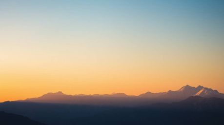 Capture the serene beauty of snow-capped mountains bathed in the soft glow of a hazy pastel sunset. This dreamy photograph fe