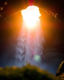 An extreme macro close-up captures a sun setting behind a dramatic waterfall, focusing on small subject detail. The image evo