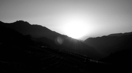 A timeless, elegant black and white photograph captures a dramatic sunset over mountainous rice terraces.  High contrast and 