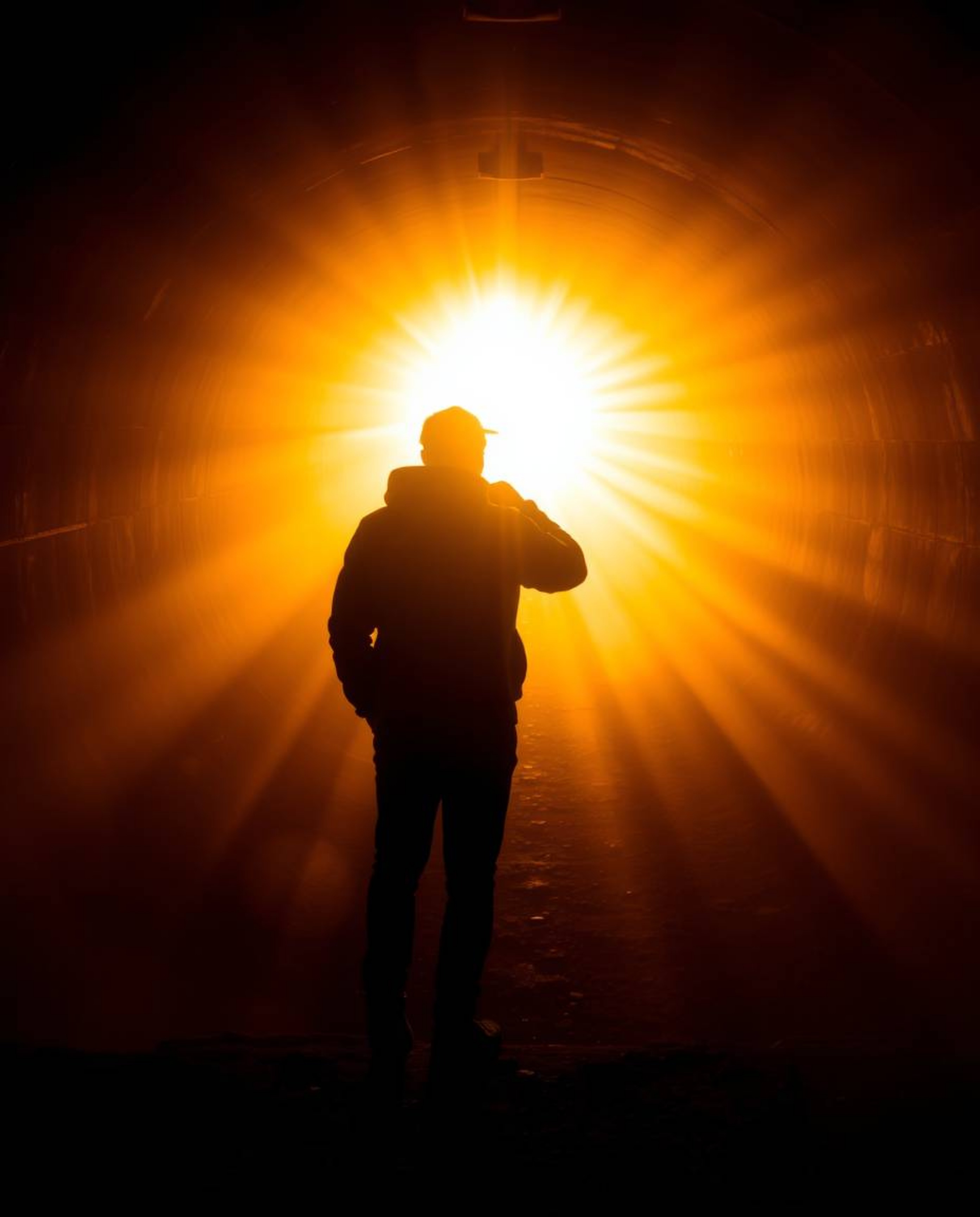 Experience the mesmerizing allure of volumetric lighting as a person stands at the tunnel's edge, gazing towards the radiant 