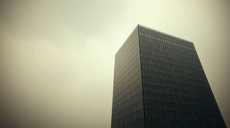 A wet, rainy scene showcases a modern glass building seamlessly dissolving into the sky, utilizing earthy tones of browns and