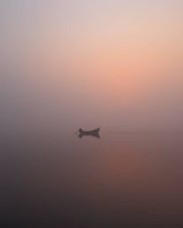 A boat gently floats on a lake during sunset, shrouded in thick fog, smooth gradient transitions depict a seamless blending o