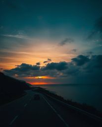 This is a high-resolution, commercial-quality stock photo capturing a sunset sky over a winding coastal highway in a strong, 