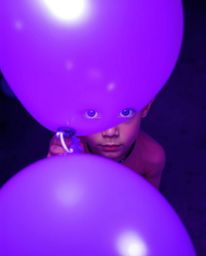 A captivating high-angle perspective captures a child with bright, expressive eyes holding a vibrant purple balloon. The imag