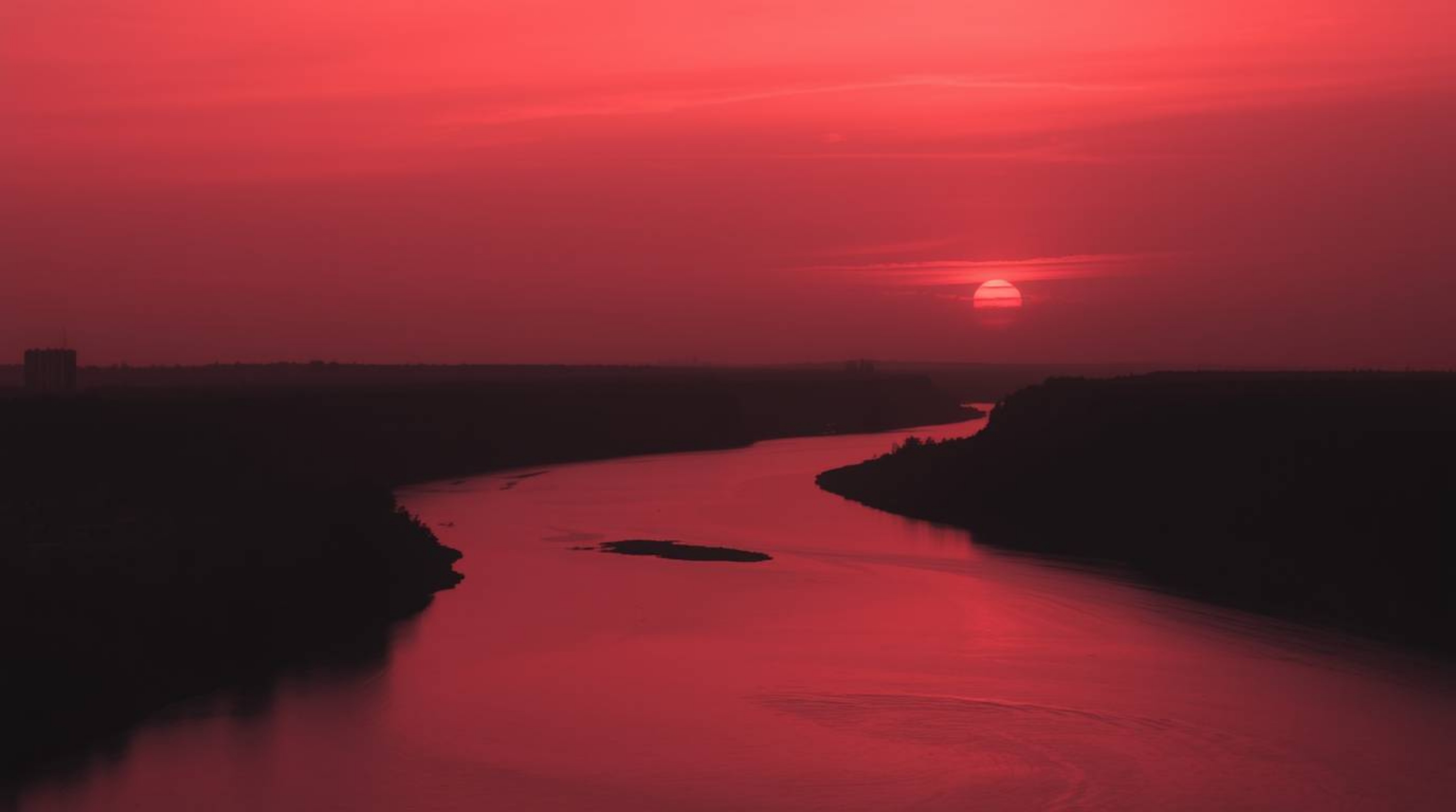 This stunning black and white photograph captures a winding river illuminated beneath a dramatic orange-pink sky. The scene i