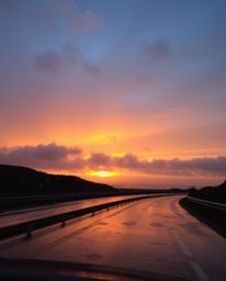 This image captures a beautifully melancholic scene of a sunset sky over a winding coastal highway under wet, rainy condition