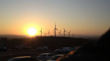 Capture the spontaneous beauty of a sunset behind wind turbines on a hill. This candid street photography close-up showcases 