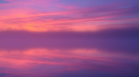 Experience the tranquility of a serene lake mirroring a vivid sunset sky, partially obscured by a thick fog. The scene is pai