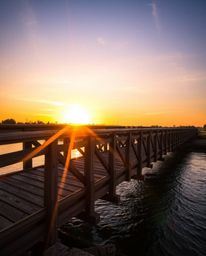A graceful and elegant image of an old wooden bridge over a river at sunset. This photograph is characterized by its vibrant 