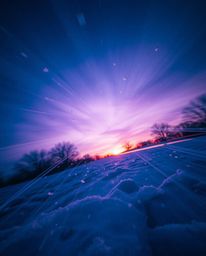 This image captures snowflakes falling during a vibrant sunset from a dramatic low-angle perspective, looking up. Using a lon