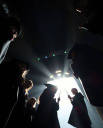 A dramatic low-angle perspective showcasing silhouetted young wizards at a magical school. The backlighting creates a stunnin
