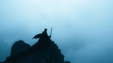 A breathtaking high-angle view captures a dragon and rider silhouetted against thick fog obscuring icy mountains below, empha