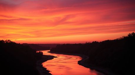 A captivating image depicts a winding river bathed in the warm glow of a dramatic orange-pink sunset.  The scene is enhanced 