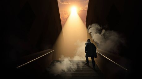 A lone figure, clad in dark clothing, ascends a weathered stone staircase bathed in a powerful beam of divine light that cuts