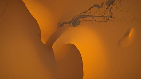 An overhead bird's eye view captures a breathtaking desert sunset scene with golden dunes glistening during a rare, wet, rain
