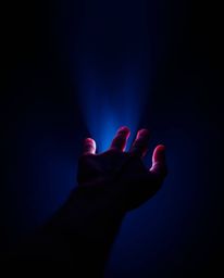 A captivating image depicting a hand reaching towards a light source emerging from darkness.  The rich burgundy and deep blue