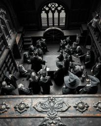 A timeless and elegant black and white image depicts a high-angle view of a magical school teeming with young wizards, cast u