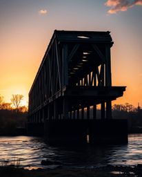 A professional, fine art photograph capturing an epic scene of an old wooden bridge over a river at sunset. This image is def