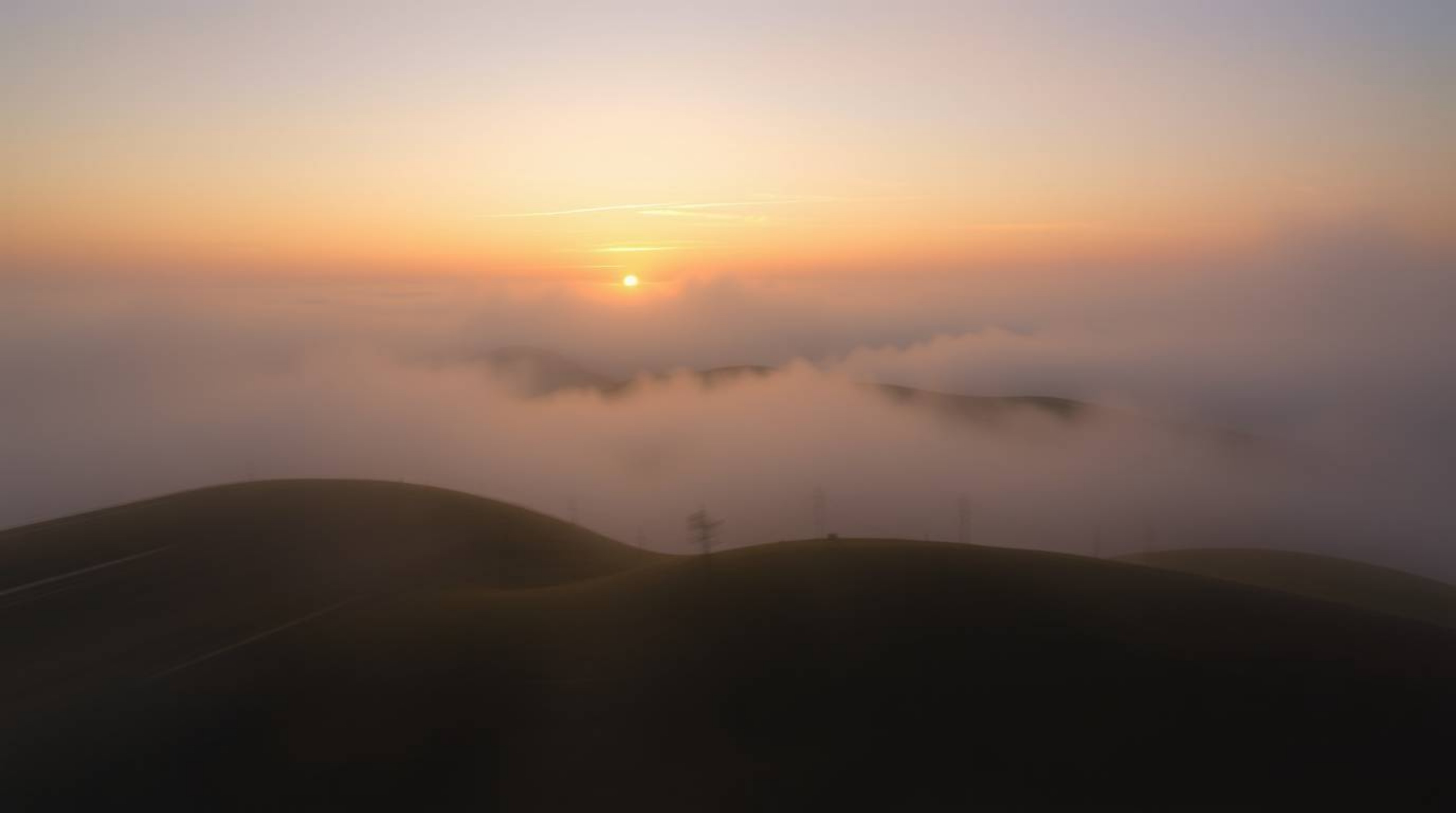 Experience a captivating dynamic motion image featuring fog-covered hills bathed in the warm glow of a setting sun.  The scen