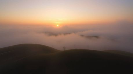 Experience a captivating dynamic motion image featuring fog-covered hills bathed in the warm glow of a setting sun.  The scen