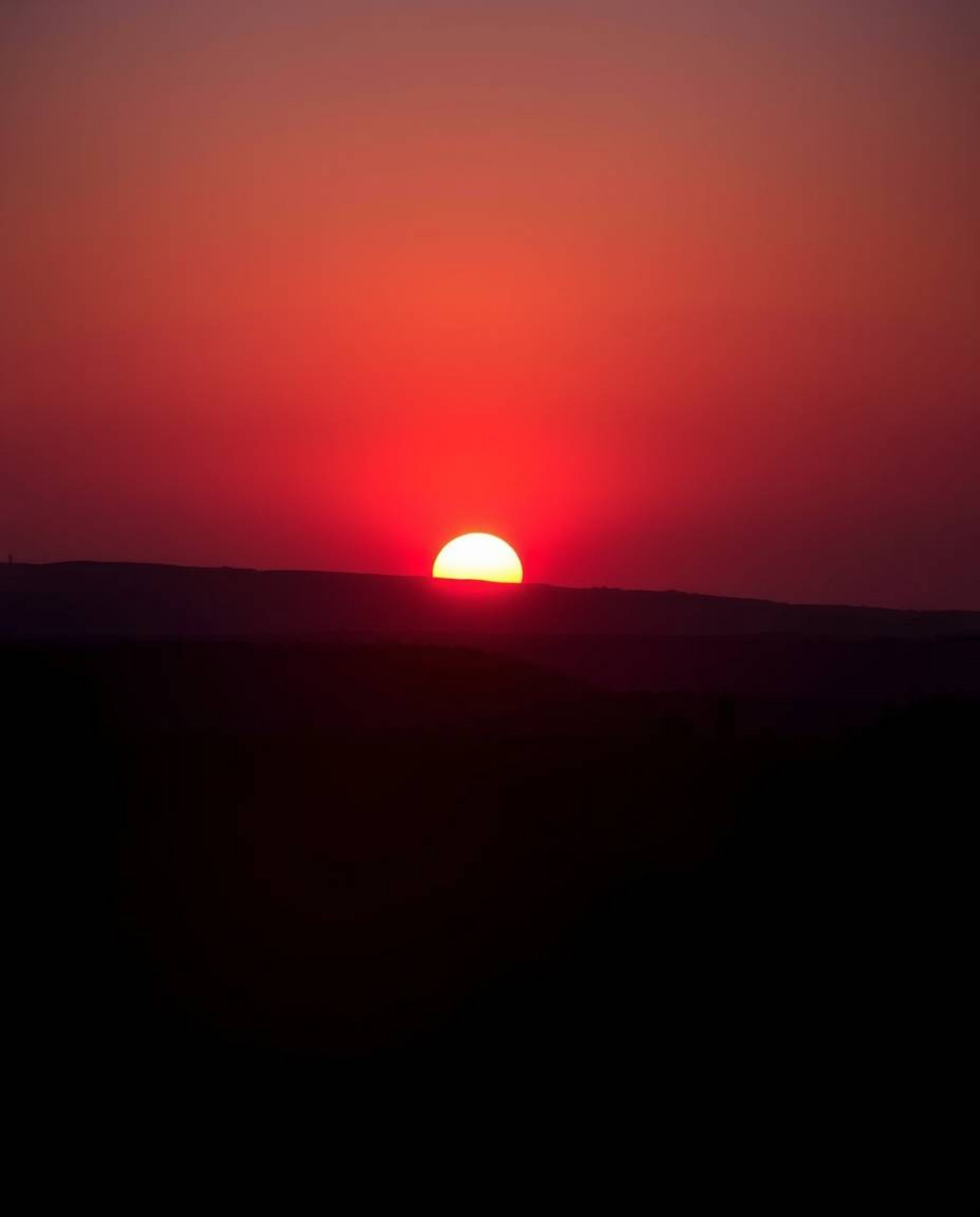 Witness a breathtaking silhouetted sunrise over a war-torn landscape, bathed in rich burgundy and deep blue hues. The backlig