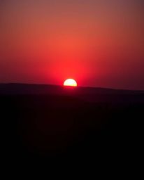 Witness a breathtaking silhouetted sunrise over a war-torn landscape, bathed in rich burgundy and deep blue hues. The backlig