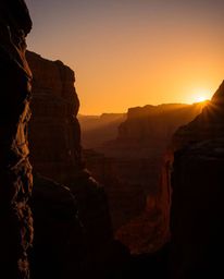 An image of a sunset illuminating sandstone cliffs in a canyon is rendered with high-contrast, low-key lighting. The scene is