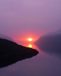 A warm, soft, professional photograph of a glassy fjord reflecting a sunset, bathed in the intimate glow of warm candlelight.