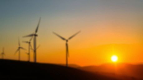 Capture the serene beauty of a sunset behind wind turbines on a hilltop with a blurred bokeh effect. This image features a sh