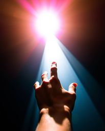 This stunning image captures a bird's eye view of a hand reaching towards a radiant light source emanating from the depths of