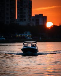 A candid street photography shot of a boat drifting on a lake at sunset. The boat is in sharp focus, while the background urb