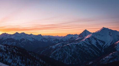A stunning high-resolution stock photo captures snow-covered mountains bathed in the warm glow of a pastel sunset.  The image