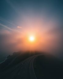 This is a bird’s-eye view of a sunset sky over a winding coastal highway. The scene is illuminated with gentle soft light and