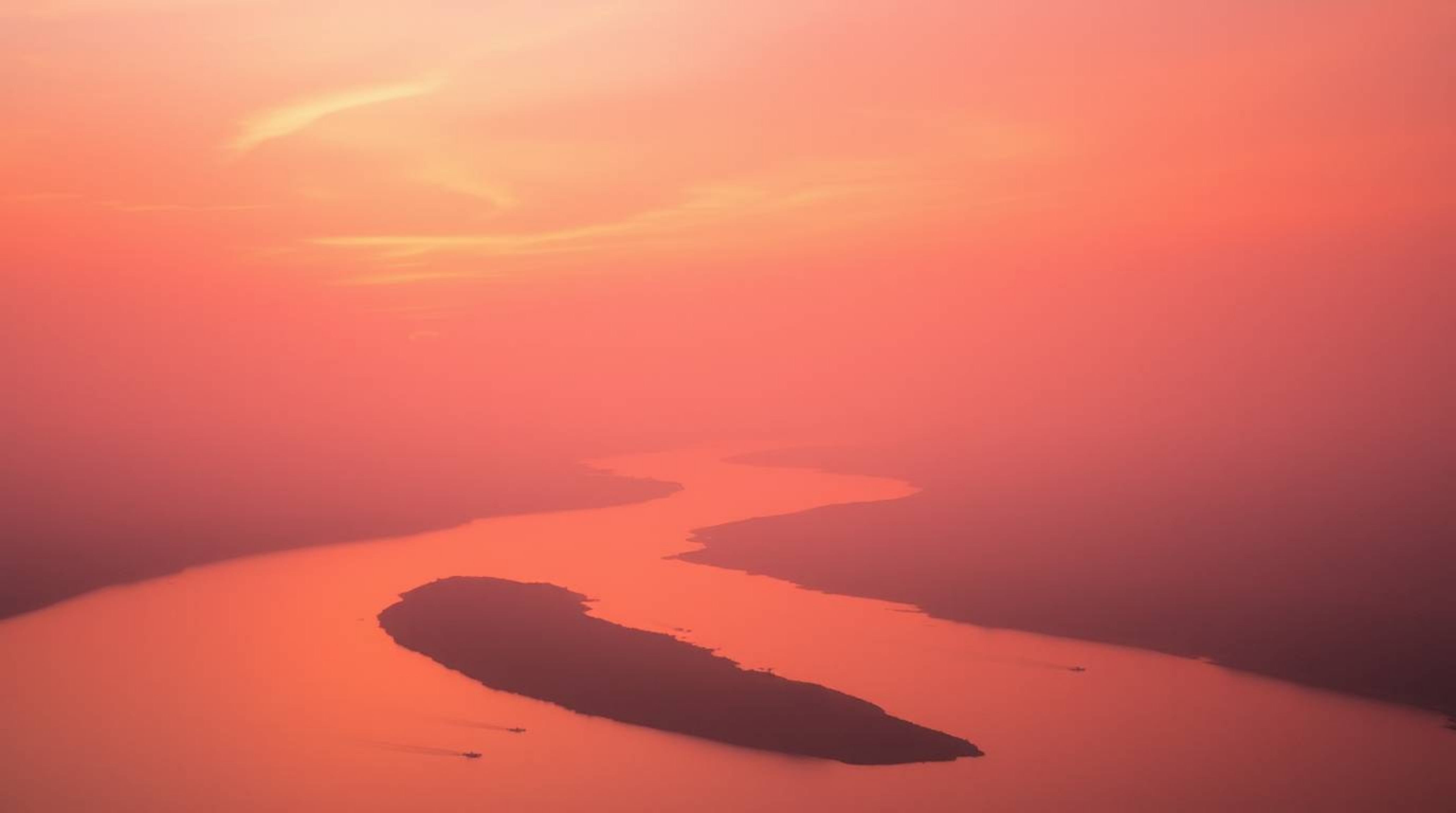 Experience the beauty of a winding river reflecting a dramatic orange-pink sunset, rendered with a soft cinematic haze and a 