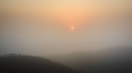Experience the ethereal beauty of foggy hills bathed in the warm glow of a breaking sunset. This image evokes a dreamy atmosp