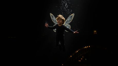 A captivating image of a young boy soaring above the London skyline, dusted with magical pixie particles.  The scene is rende