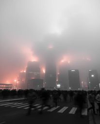 A long exposure photograph captures a city engulfed in flames, with thick fog obscuring the finer details. The scene depicts 