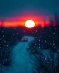An unusual and original fine art photograph captures the scene of snowflakes falling during a vibrant sunset. This piece is d