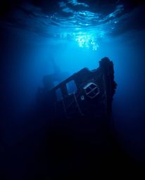 A dramatic underwater scene featuring a shipwreck illuminated with high contrast, low key lighting. Cool blues, greens, and p