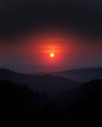 This is a moody digital painting capturing a Tuscan sunset over misty, rolling hills from a high-angle, elevated viewpoint. T