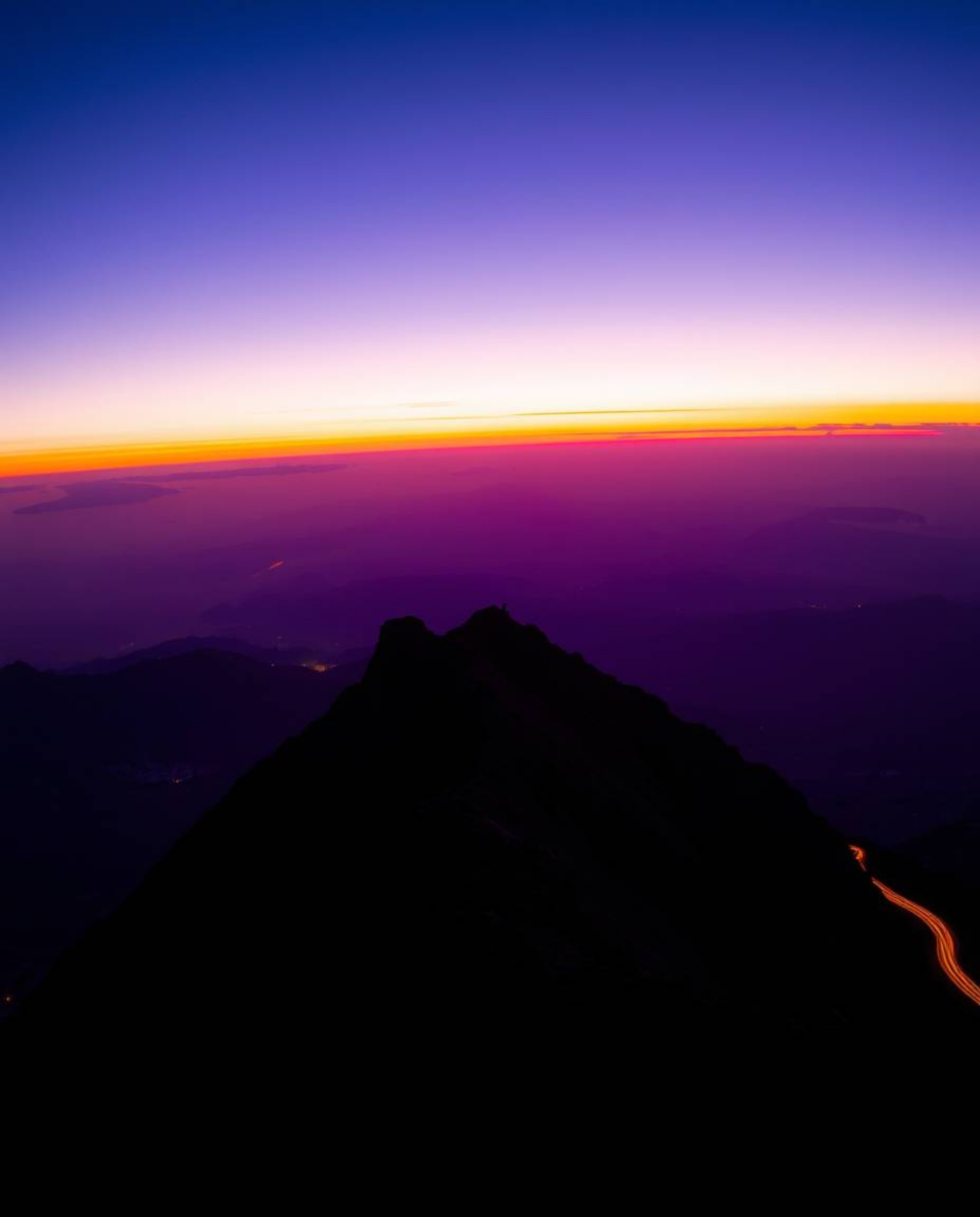 This stunning long-exposure photograph captures a sunset from a high alpine peak, rendered in deep ultraviolet hues and vivid
