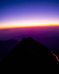 This stunning long-exposure photograph captures a sunset from a high alpine peak, rendered in deep ultraviolet hues and vivid