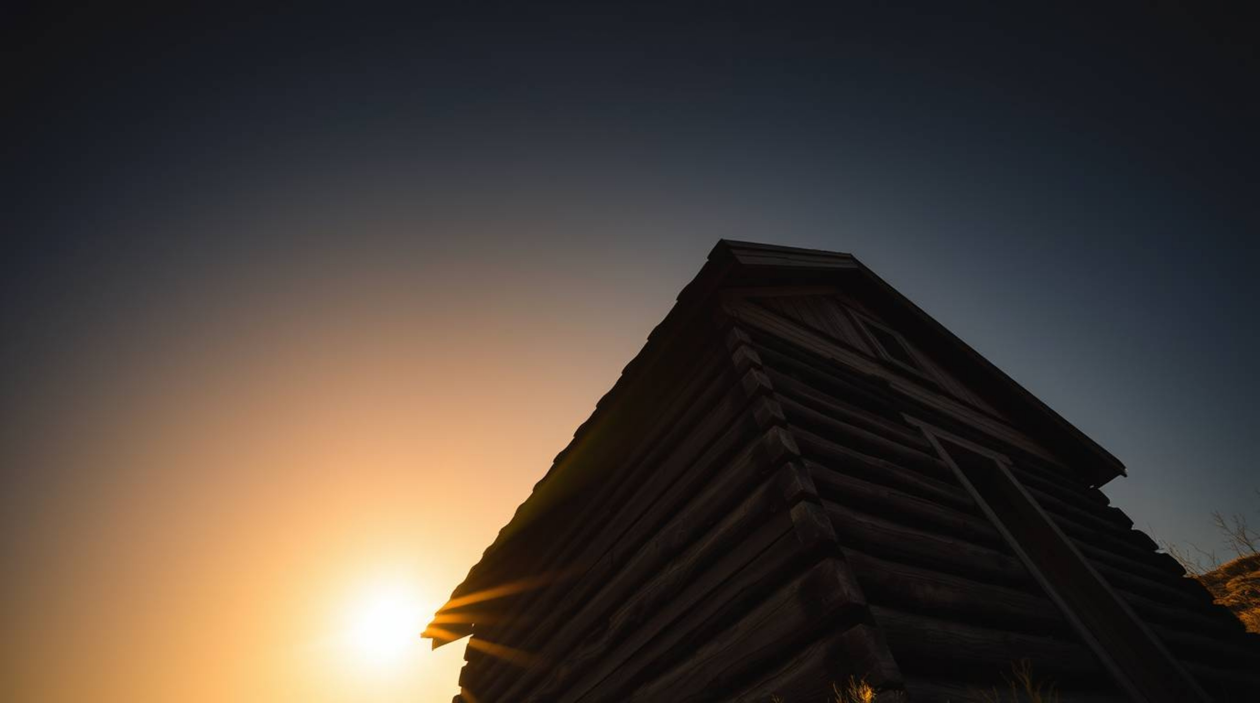 A captivating image showcasing an old wooden cabin bathed in the dramatic, low-angle light of sunset.  The high contrast and 