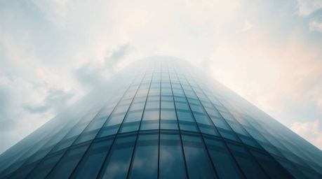 A captivating low-angle photograph showcases a modern glass building seemingly dissolving into the sky, its structure seamles