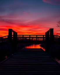 An extreme macro close-up captures the intricate details of an old wooden bridge over a river at sunset. The image is rendere