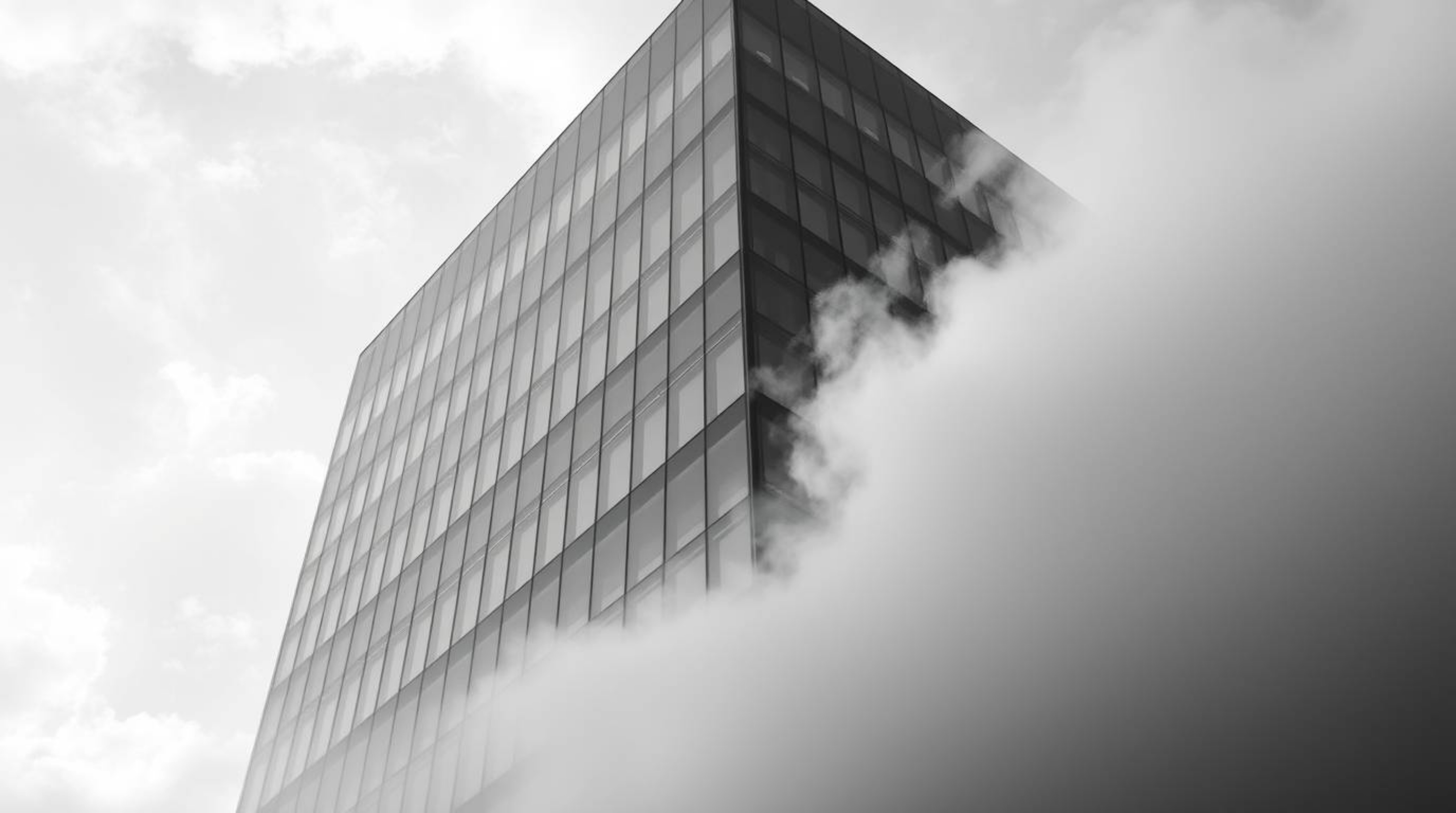 A captivating black and white photograph showcases a modern glass building seemingly dissolving into the soft clouds above, c