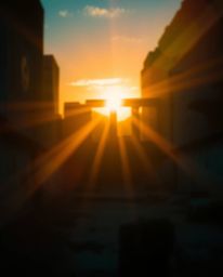 A blurred bokeh effect with bright lens flare highlights a sunset casting shadows through ancient stone ruins. The image show