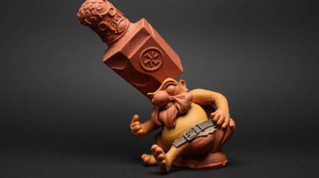 This striking clay sculpture depicts a dramatic scene: an anvil poised to fall upon a trickster character.  The artwork featu