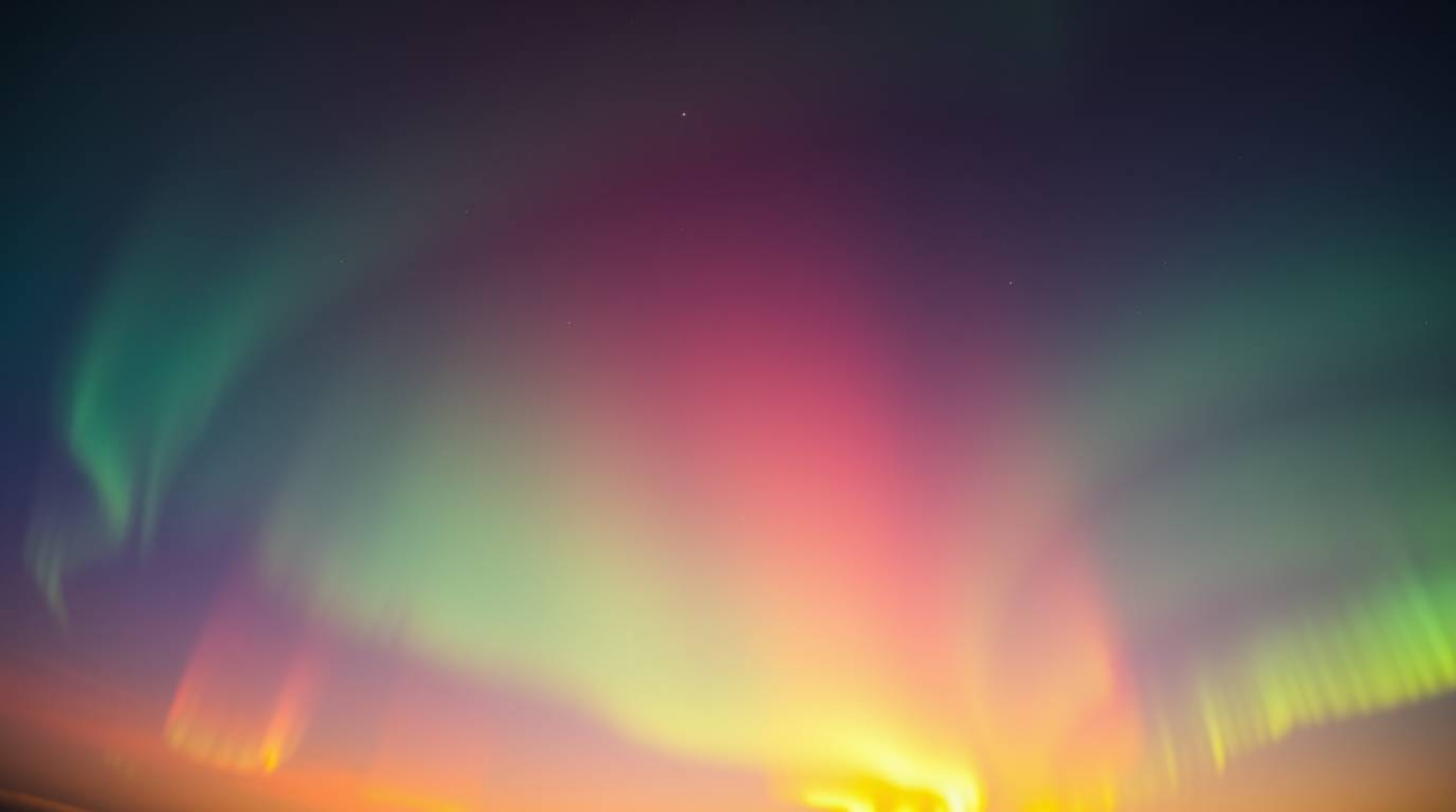 Witness the magical display of the Aurora Borealis as it emerges over a vibrant sunset sky in this tight close-up shot. Irid