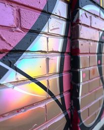 This striking image showcases elegant iridescent reflections dancing across graffiti-style colorful splashes on a brick wall.